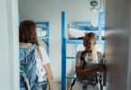 Two women with backpacks walking into a bright hostel dormitory with bunk beds, ready for adventure.