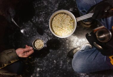 Two people preparing and serving rice outdoors from a pot on a cold day.