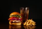 Juicy cheeseburger with fries and a refreshing drink on a dark background.