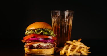 Juicy cheeseburger with fries and a refreshing drink on a dark background.