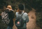 Two friends explore a forest trail together with backpacks, enjoying nature.