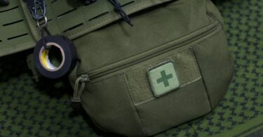 Close-up of a green first aid kit pouch attached to military gear, highlighting preparedness.